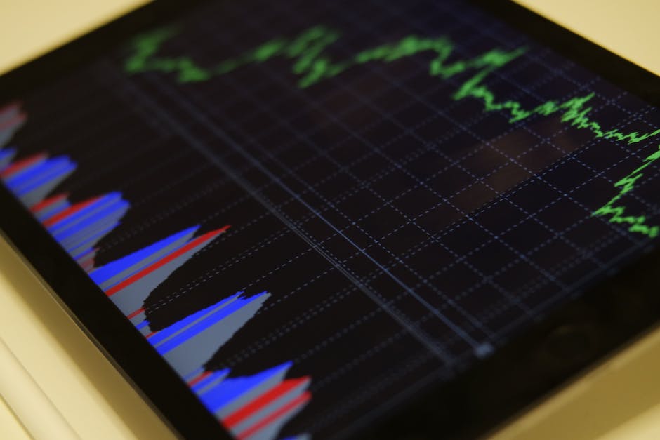 An image of a person using a computer to analyze stocks in a graph form, with green and red lines plotted out.