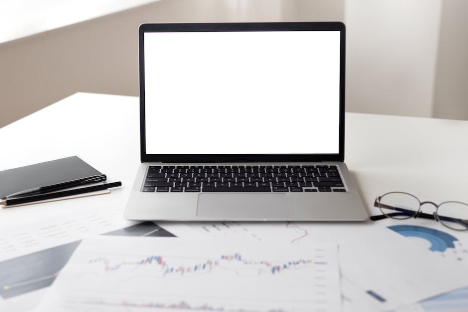 A person sitting at a desk with a computer, a cup of coffee, and papers with charts on them, representing stock trading platforms.